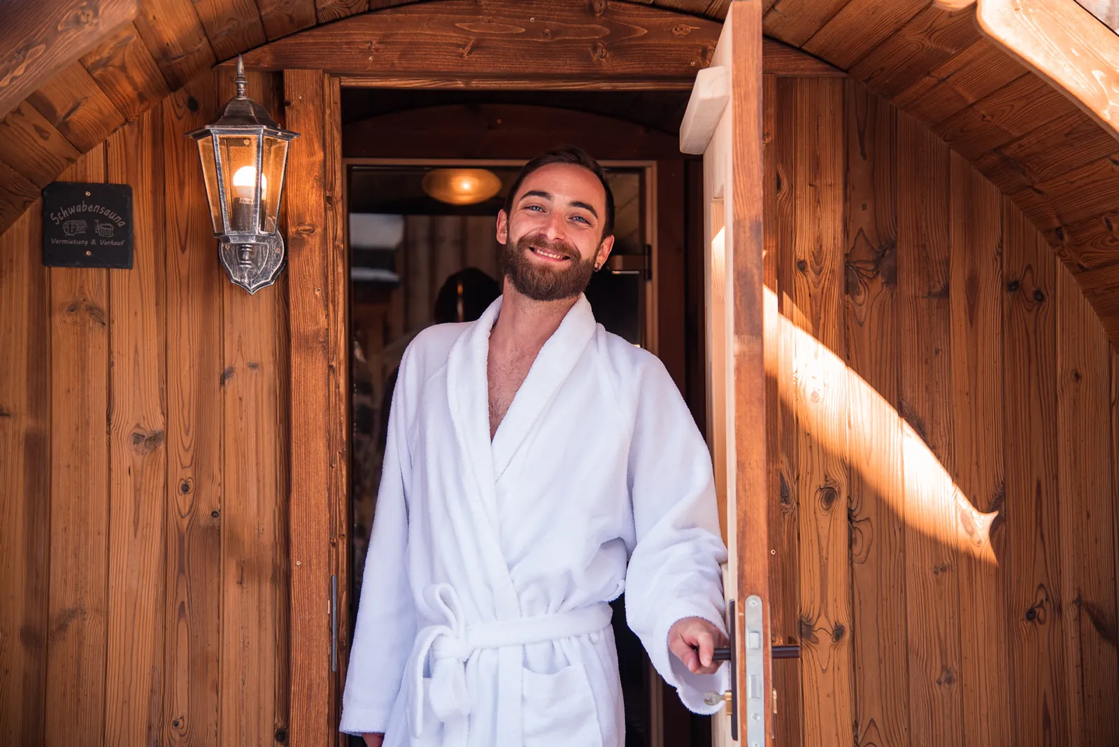 Gast im Bademantel an der Tür der Fasssauna