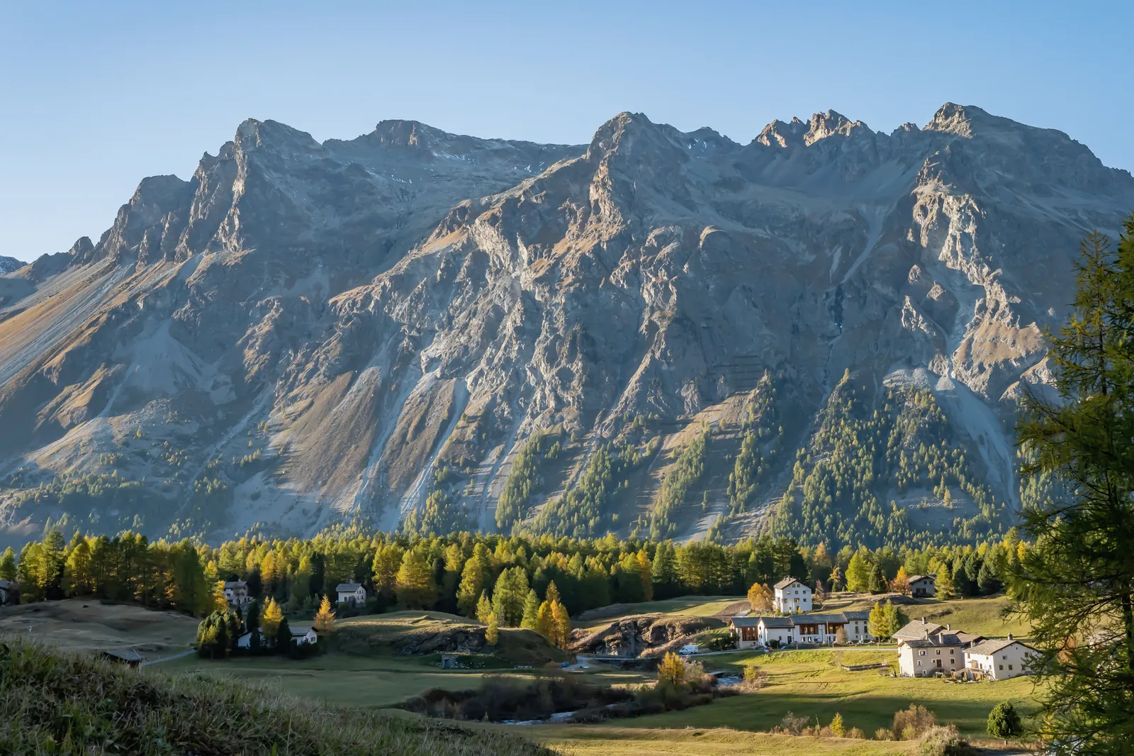 Das Val Fex im Herbst, Lärchen und Weiler unter der Felswand